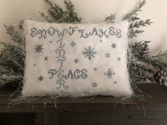 Photo of finished pillow tuck from Snowflakes by Falling Star Primitives, displayed on top of evergreen branches